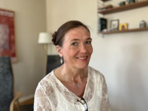 Porträttbild av Jenny Anne sitter hemma i sitt kök och tittar in i kameran och ler.